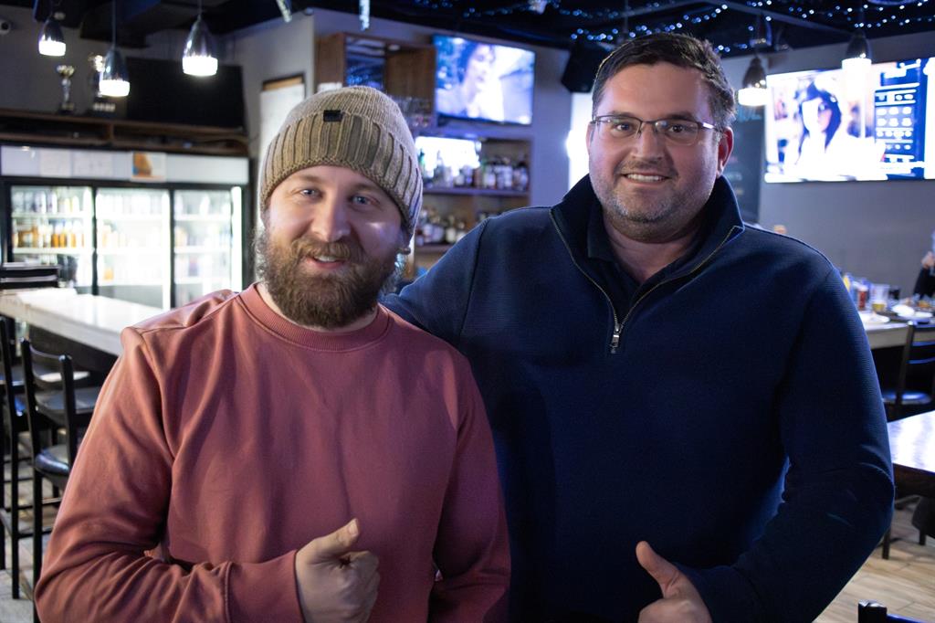 Man in red sweater next to man in blue sweater in a restaurant